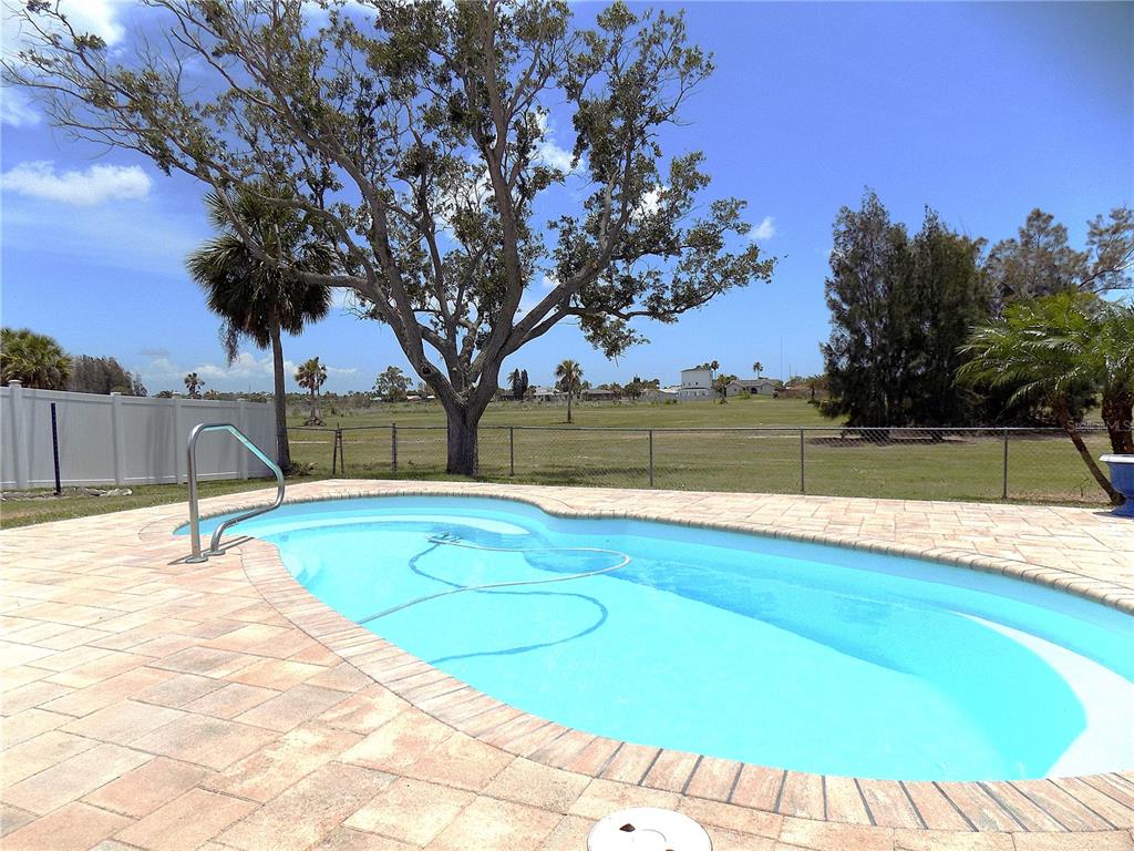 A swimming pool with a paved deck sits in a backyard with a large tree — 3842 HEADSAIL DRIVE, NEW PORT RICHEY, FL