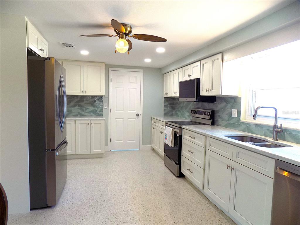 A kitchen with white cabinets, stainless steel appliances, a tiled backsplash, and a ceiling fan — 3842 HEADSAIL DRIVE, NEW PORT RICHEY, FL