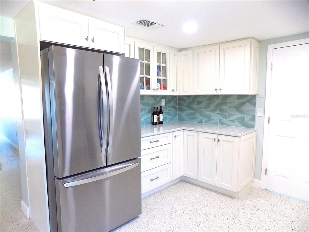 A kitchen features white cabinets, stainless steel appliances, and a green tiled backsplash — 3842 HEADSAIL DRIVE, NEW PORT RICHEY, FL