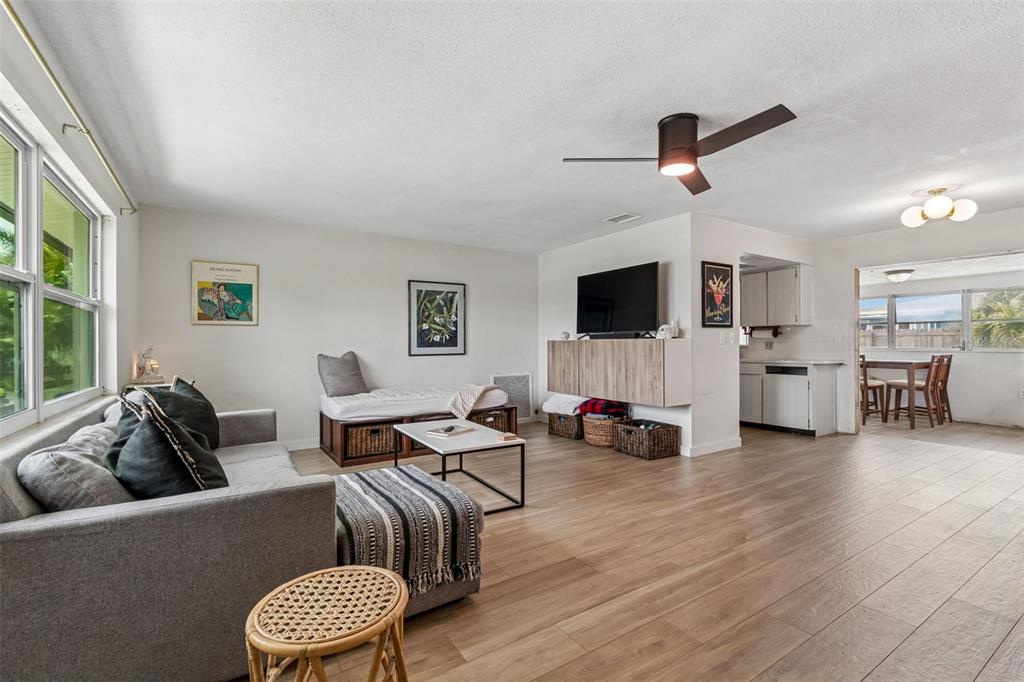 A living room with light wood-look flooring, a grey sofa, and an open kitchen area — 11555 63RD AVENUE, SEMINOLE, FL