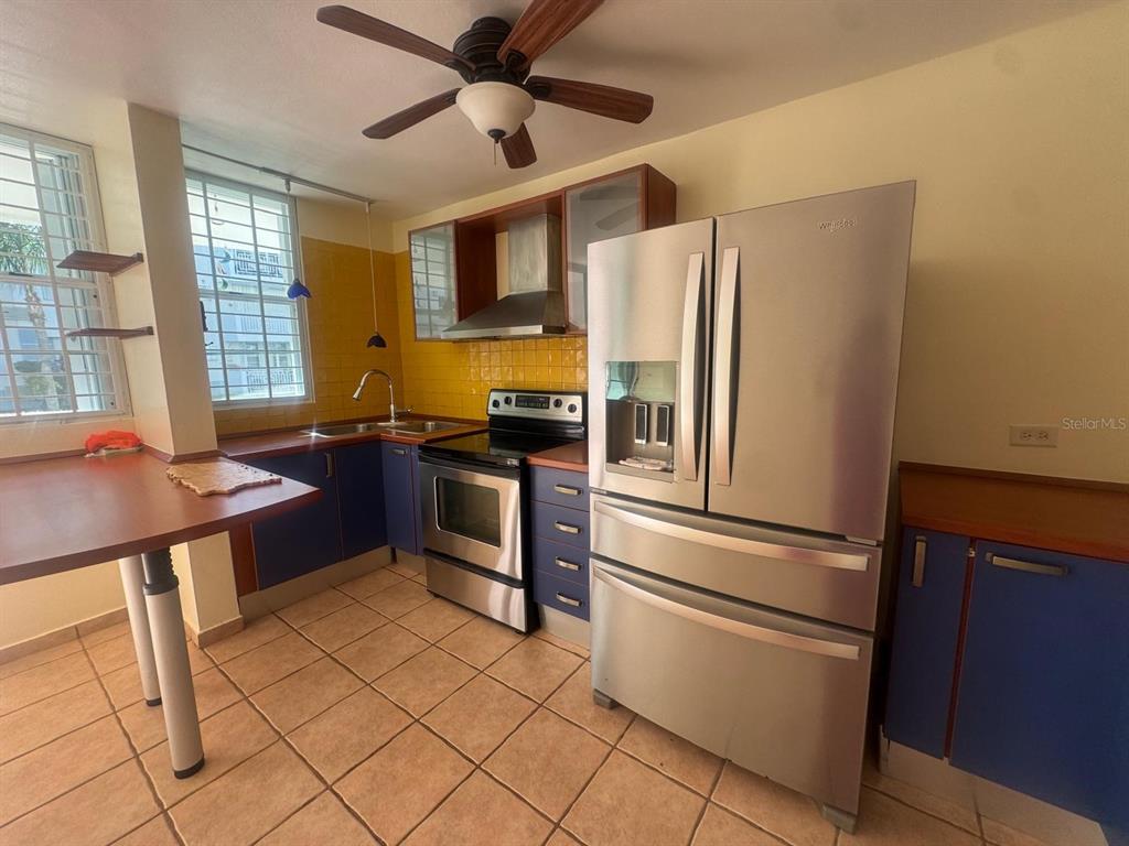 A kitchen with blue cabinets, yellow tile backsplash, stainless steel appliances, and a ceiling fan — II LOS PARILLAS UNIT 3501, LOIZA, PR
