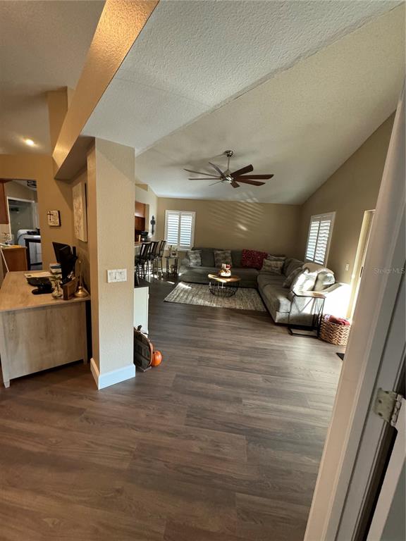 A living room with wood-look flooring, a sectional sofa, and a vaulted ceiling with fan — 28508 MEADOWRUSH WAY, WESLEY CHAPEL, FL