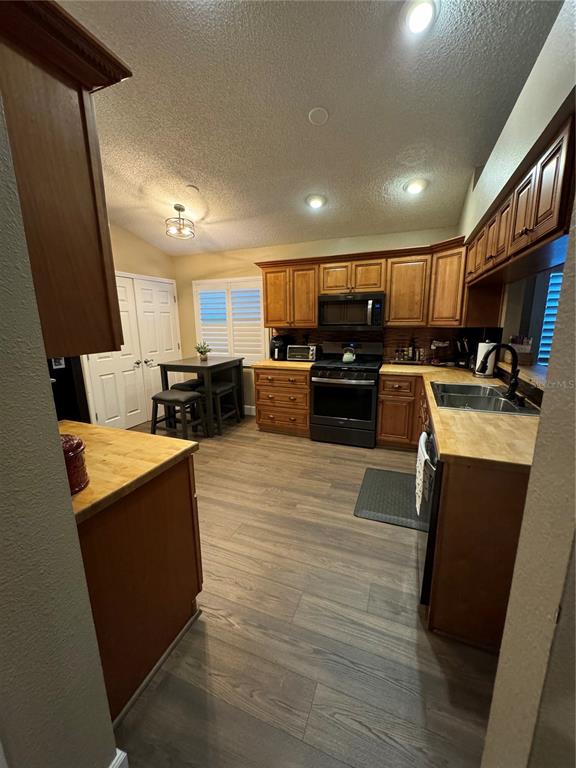 A kitchen features wood cabinets, butcher block countertops, stainless steel appliances, and wood-look flooring — 28508 MEADOWRUSH WAY, WESLEY CHAPEL, FL