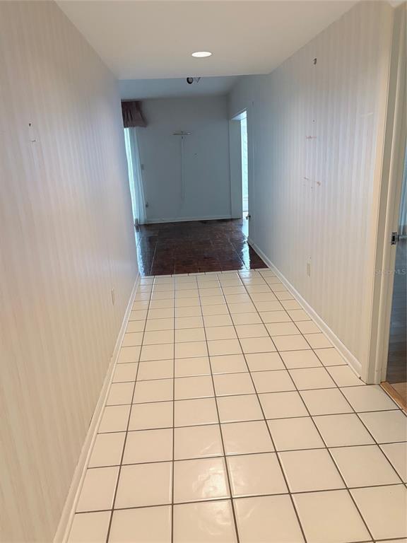 A hallway with white tiled flooring leads to a room with dark wood-look flooring — 14111 CYPRESS CIRCLE, TAMPA, FL