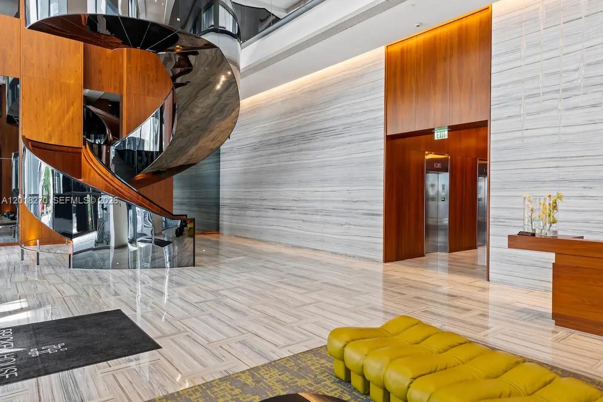 A modern lobby features a spiral staircase, marble floors, wood paneling, and a yellow bench — 1300 Brickell Bay Dr # 2000, Miami FL 33131, MIAMI, FL