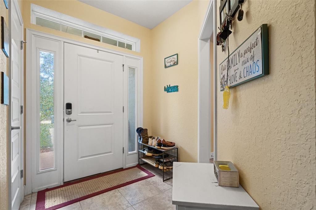 A tiled entryway features a white front door with sidelights, a shoe rack, and yellow walls — 18336 MACEK ROAD, WEEKI WACHEE, FL