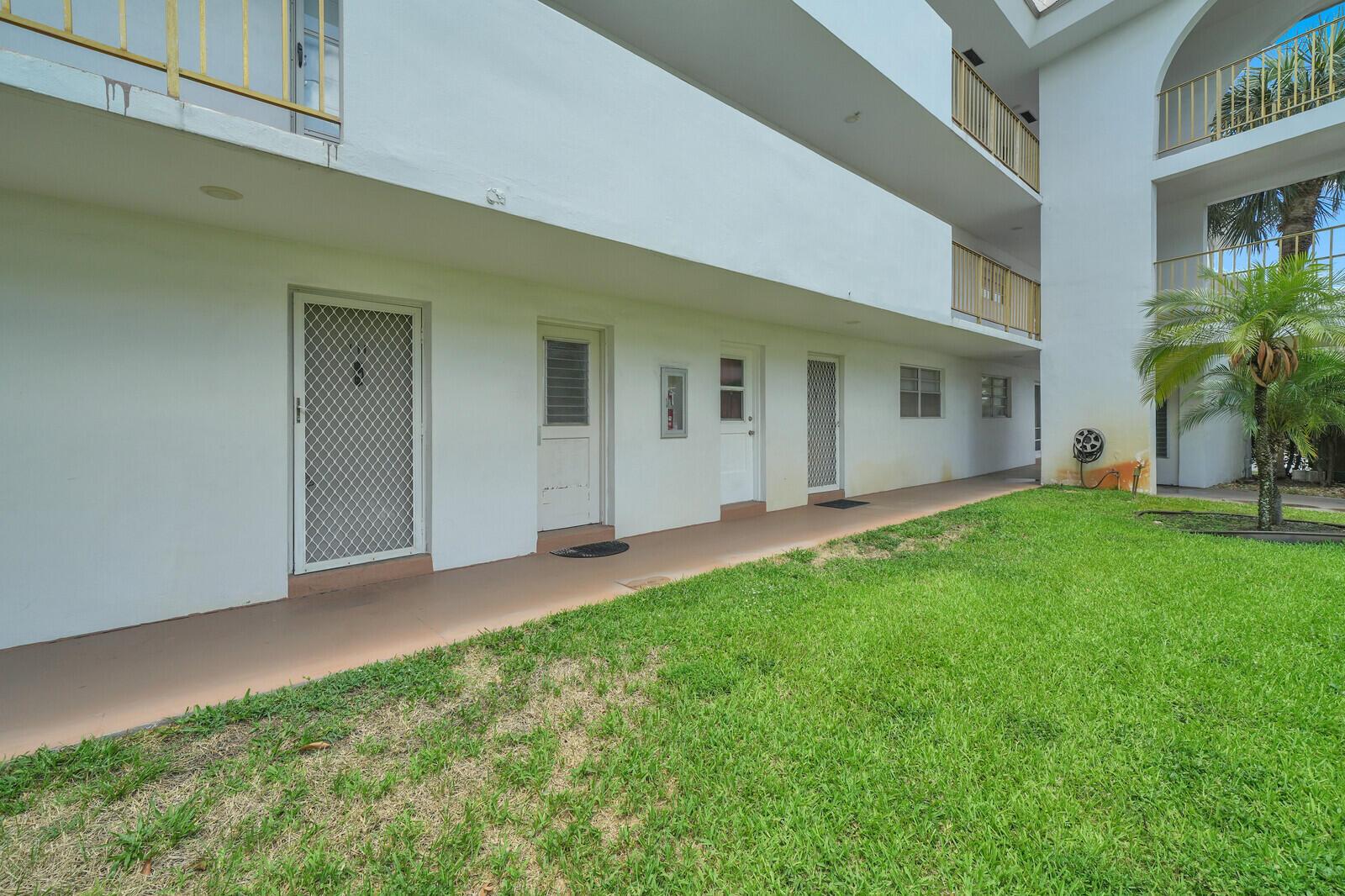 A three-story white apartment building with exterior walkways overlooks a grassy courtyard with palm trees — 5501 NW 2nd Avenue # 111, Boca Raton FL 33487, BOCA RATON, FL
