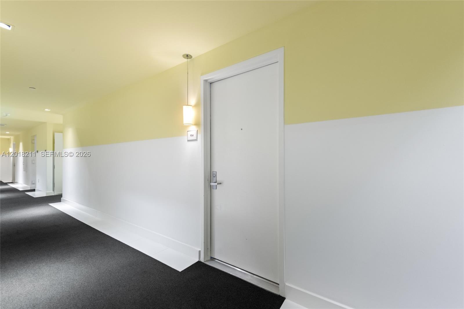 A hallway with white and yellow walls, dark carpet, and a white door — 465 Brickell Ave # 904, Miami FL 33131, MIAMI, FL