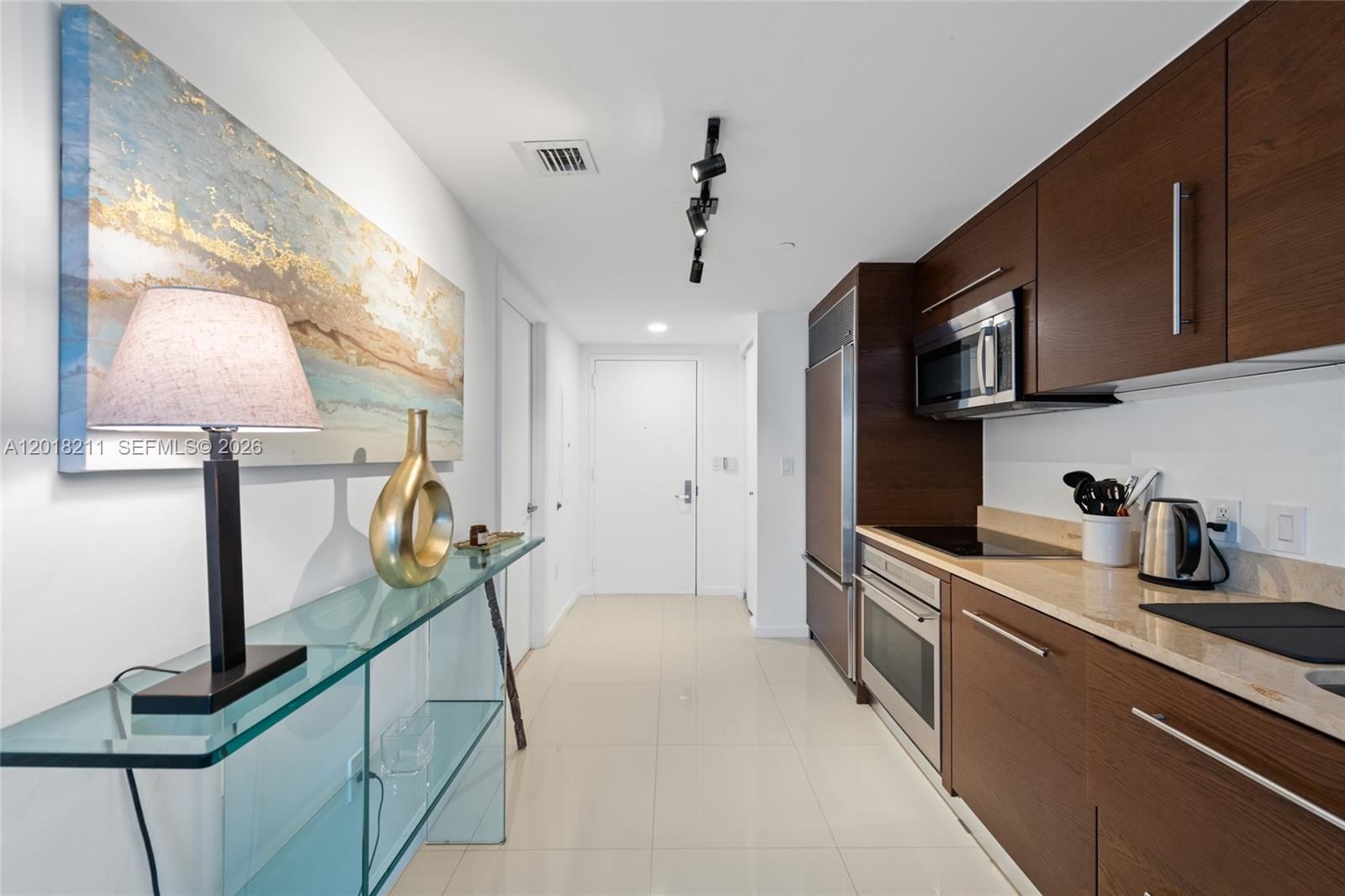 A modern kitchen features dark wood cabinetry, stainless steel appliances, and a glass console table — 465 Brickell Ave # 904, Miami FL 33131, MIAMI, FL