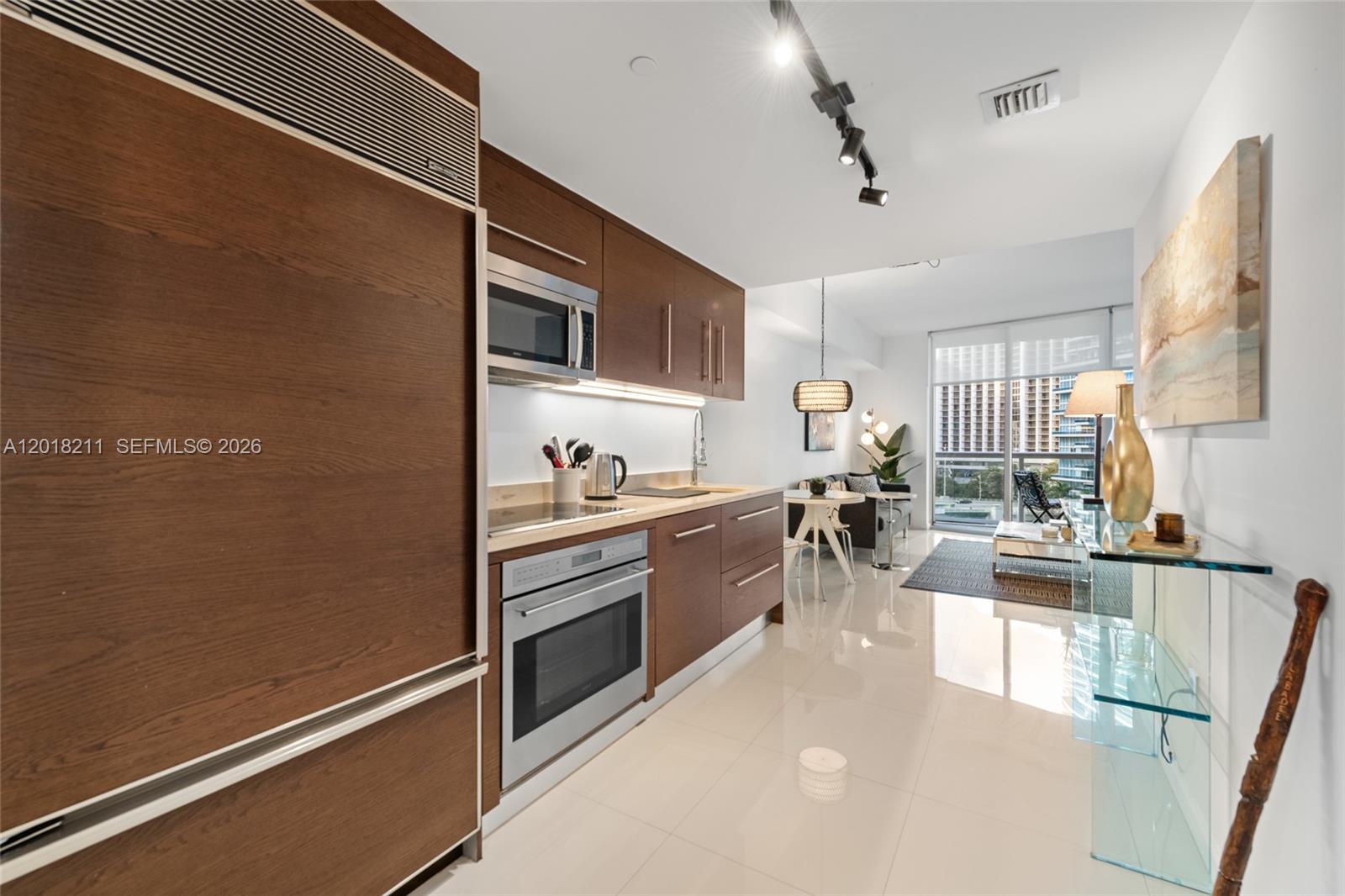 A modern kitchen with wood cabinetry and stainless steel appliances opens into a living area — 465 Brickell Ave # 904, Miami FL 33131, MIAMI, FL