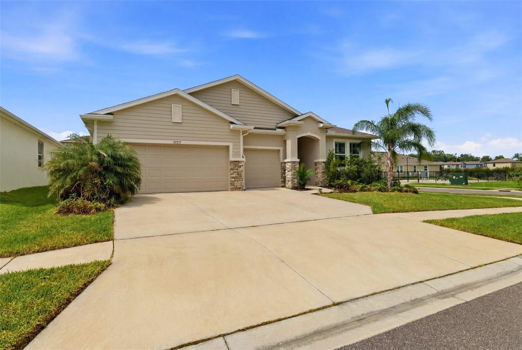 A single-story suburban house features a tan exterior, stone accents, and a three-car garage — 32337 CONCHSHELL SAIL STREET, WESLEY CHAPEL, FL