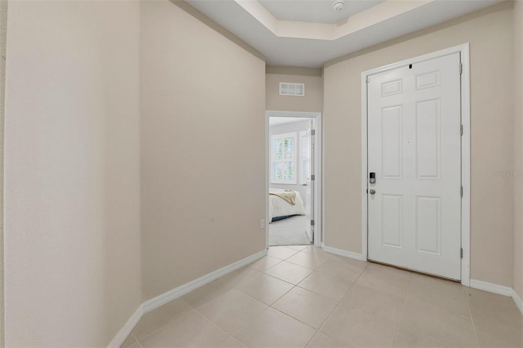 An entryway with beige walls, tile flooring, a tray ceiling, and a white front door — 32337 CONCHSHELL SAIL STREET, WESLEY CHAPEL, FL