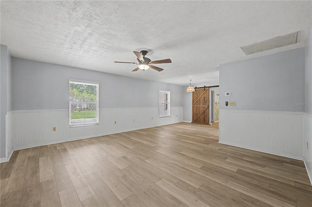 A spacious room features light wood-look flooring, white wainscoting, a ceiling fan, and a barn door — 5242 COUNTY LINE ROAD, LAKELAND, FL