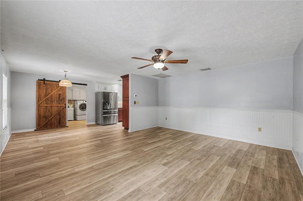 A spacious room features light wood-look flooring, white wainscoting, a ceiling fan, and a barn door — 5242 COUNTY LINE ROAD, LAKELAND, FL