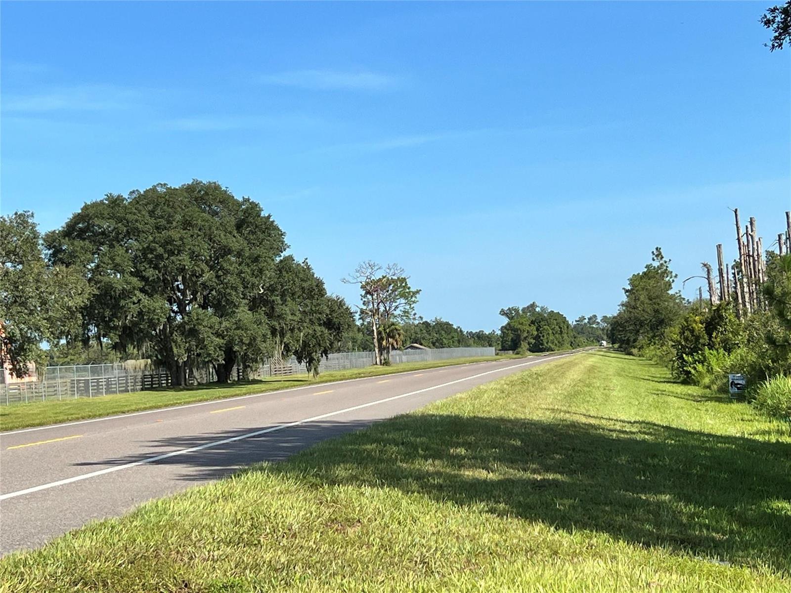 A paved road stretches into the distance past a grassy shoulder and large oak trees — 34964 N Hwy 441, Okeechobee FL 34972, OKEECHOBEE, FL