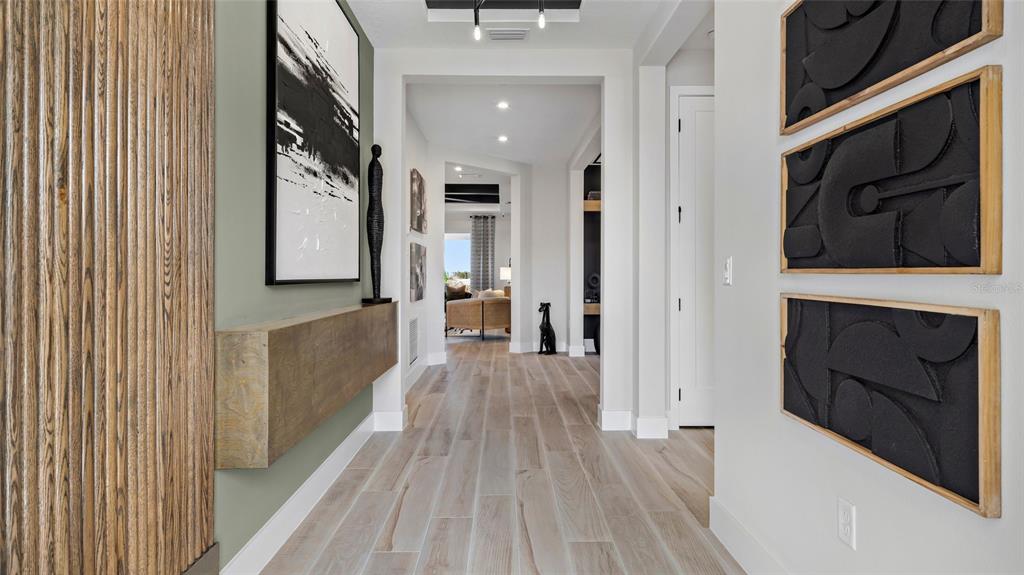 A hallway features light wood-look tile flooring, a floating wooden console, and modern wall art — 1736 POINT GRACE ROAD, TAVARES, FL