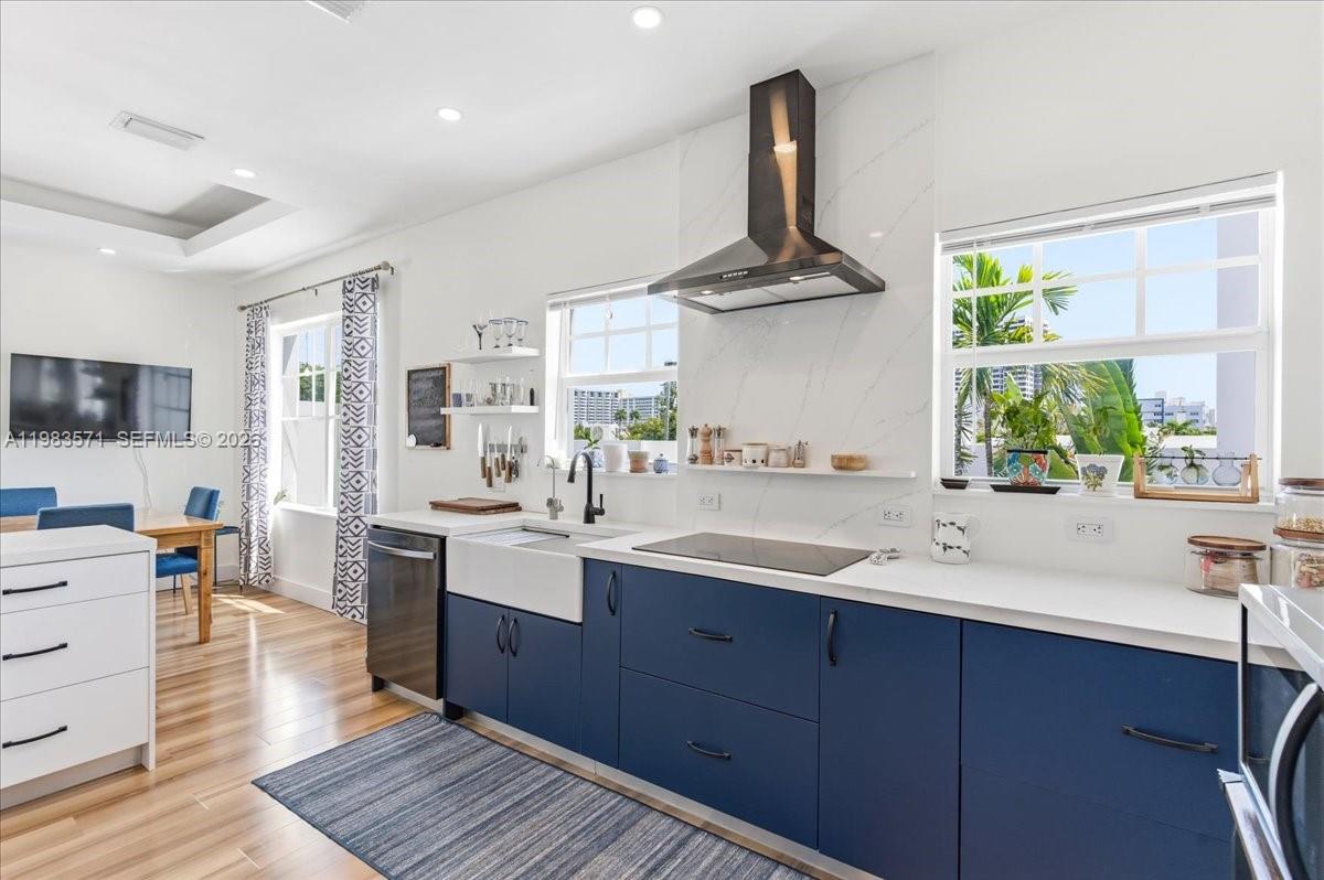 A kitchen features blue cabinets, a white farmhouse sink, and a stainless steel range hood — 2463 Pine Tree Dr PH, Miami Beach FL 33140, MIAMI BEACH, FL