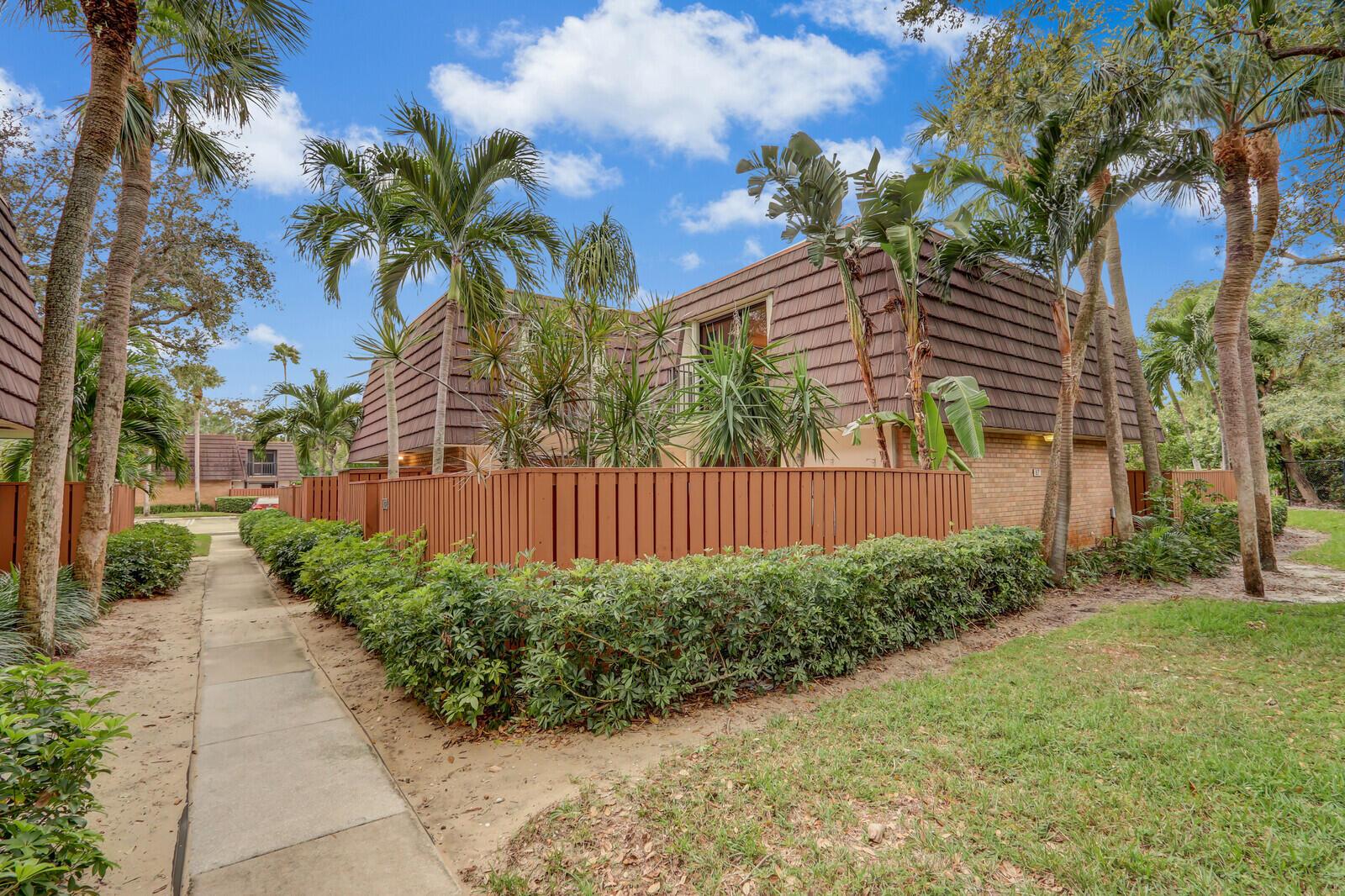 A two-story townhouse with a brown mansard roof, wooden fence, and surrounding palm trees — 1138 11th Court, Jupiter FL 33477, JUPITER, FL