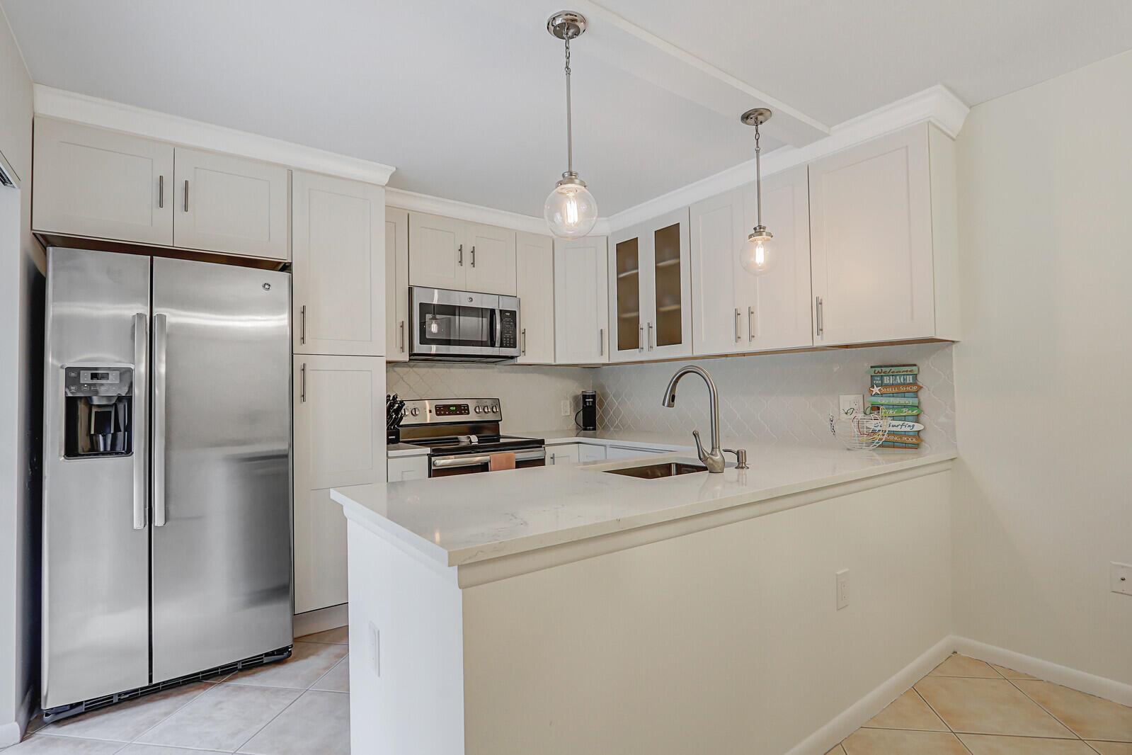 A kitchen with white cabinets, stainless steel appliances, and a quartz-topped peninsula island — 1138 11th Court, Jupiter FL 33477, JUPITER, FL