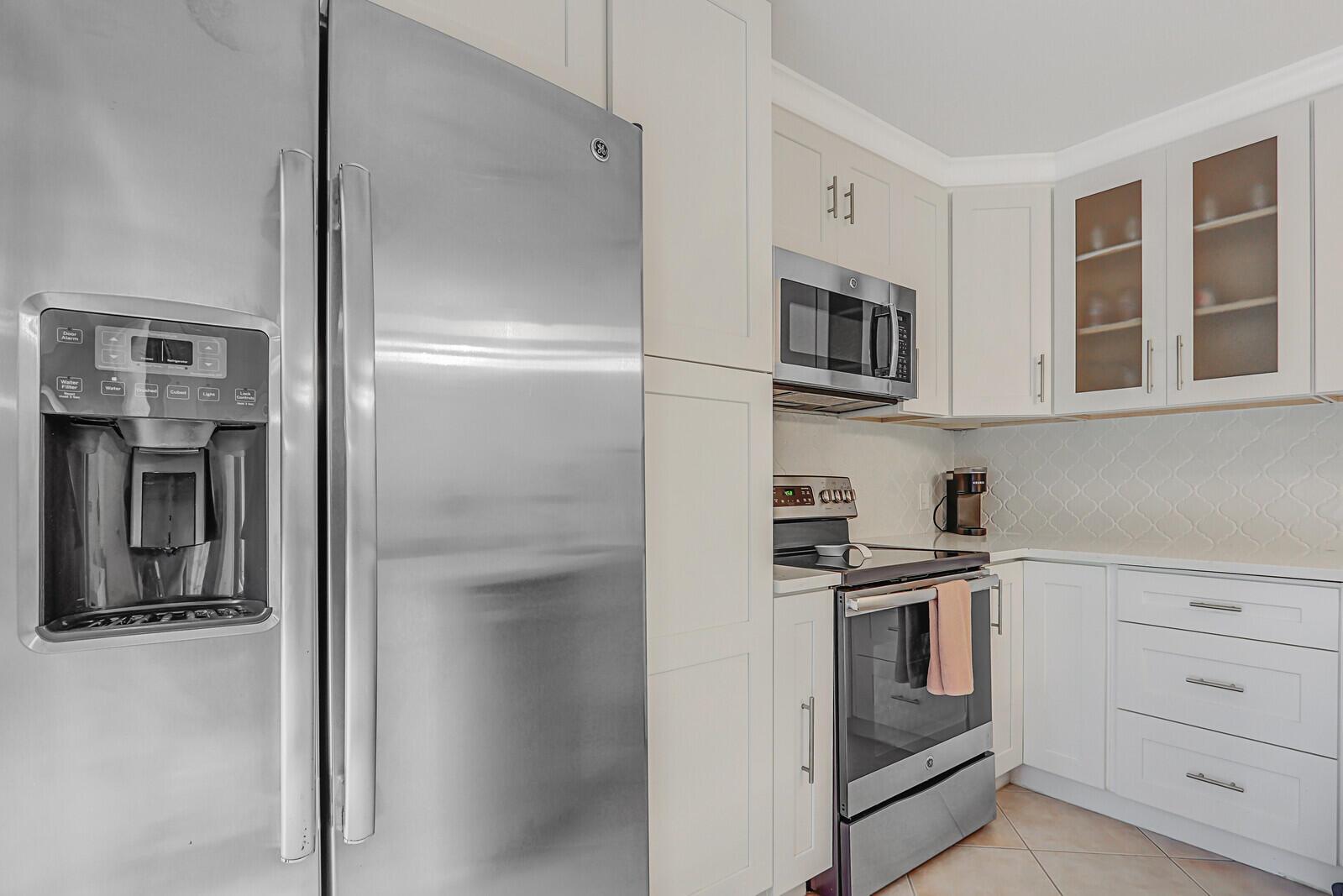 A modern kitchen features stainless steel appliances, white cabinetry, and a light-colored tile floor — 1138 11th Court, Jupiter FL 33477, JUPITER, FL