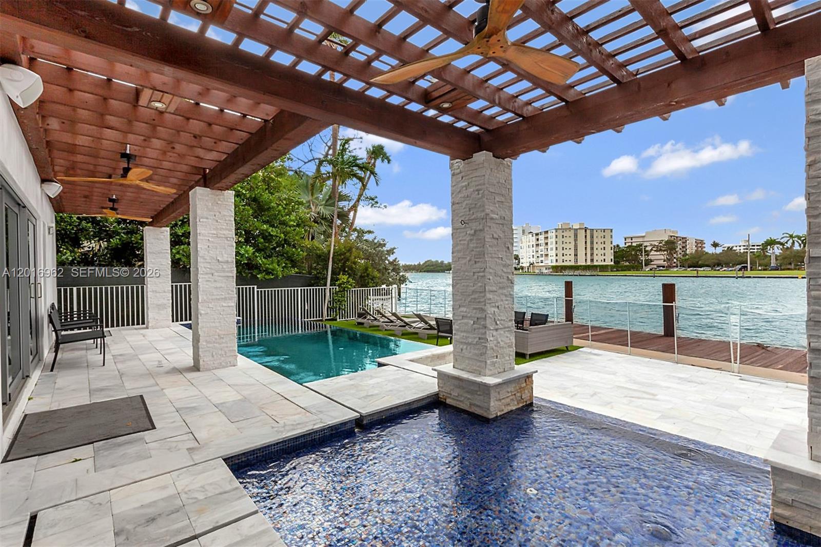 A patio with a pergola, two pools, and a view of the water and buildings — 9380 Bay Drive, Surfside FL 33154, SURFSIDE, FL