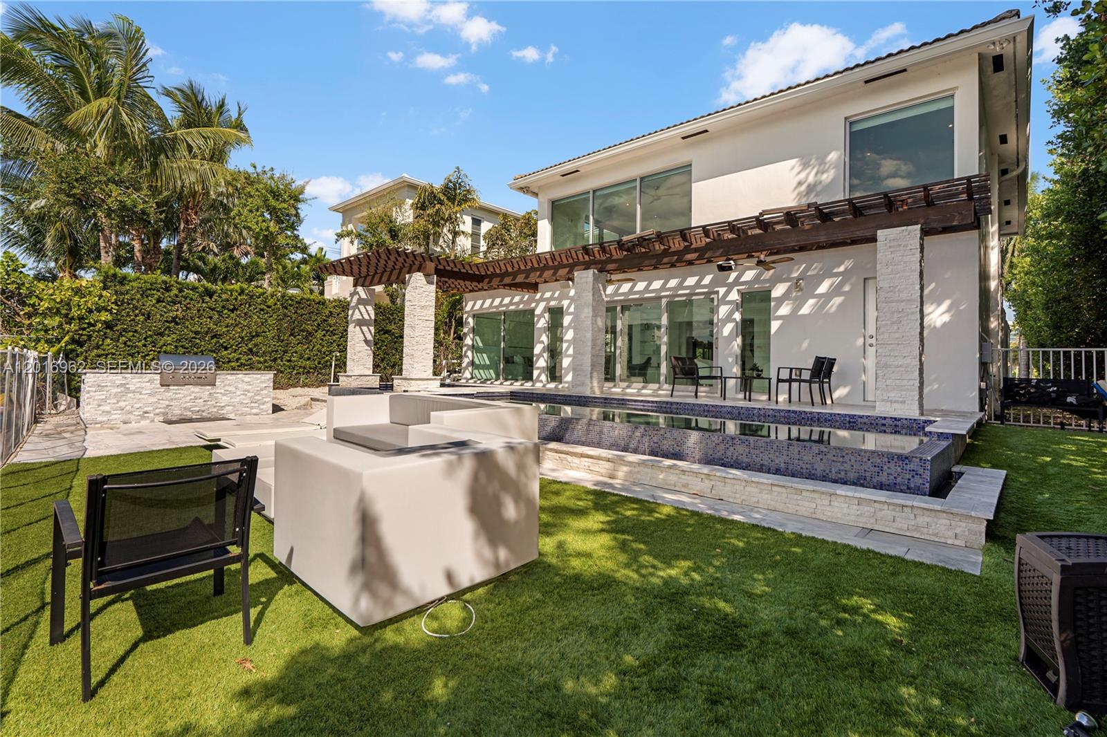 A modern two-story house features a backyard with a swimming pool, pergola, and patio furniture — 9380 Bay Drive, Surfside FL 33154, SURFSIDE, FL
