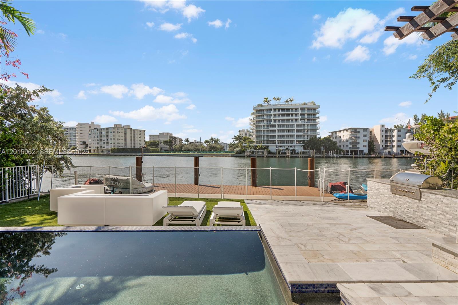 A backyard features a swimming pool, patio, lounge furniture, and a dock overlooking the water — 9380 Bay Drive, Surfside FL 33154, SURFSIDE, FL