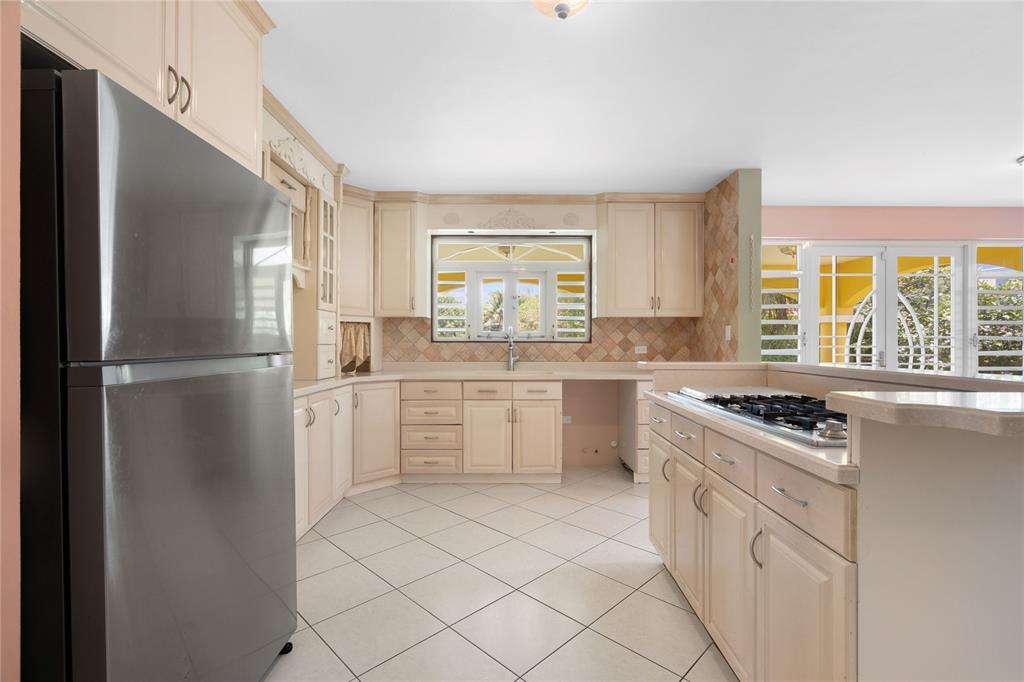 A kitchen with light-colored cabinets, a stainless steel refrigerator, a gas cooktop, and tile flooring — CEIBA NORTE QUINTAS DE VALLE VERDE, JUNCOS, PR