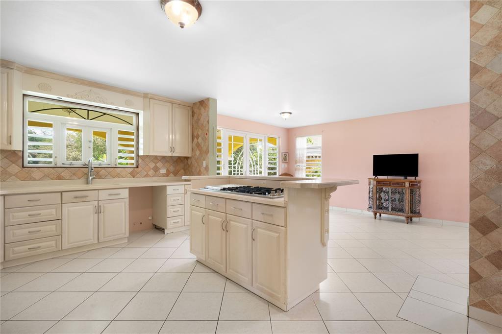 A kitchen with cream cabinets, a central island with a cooktop, and light tile flooring — CEIBA NORTE QUINTAS DE VALLE VERDE, JUNCOS, PR