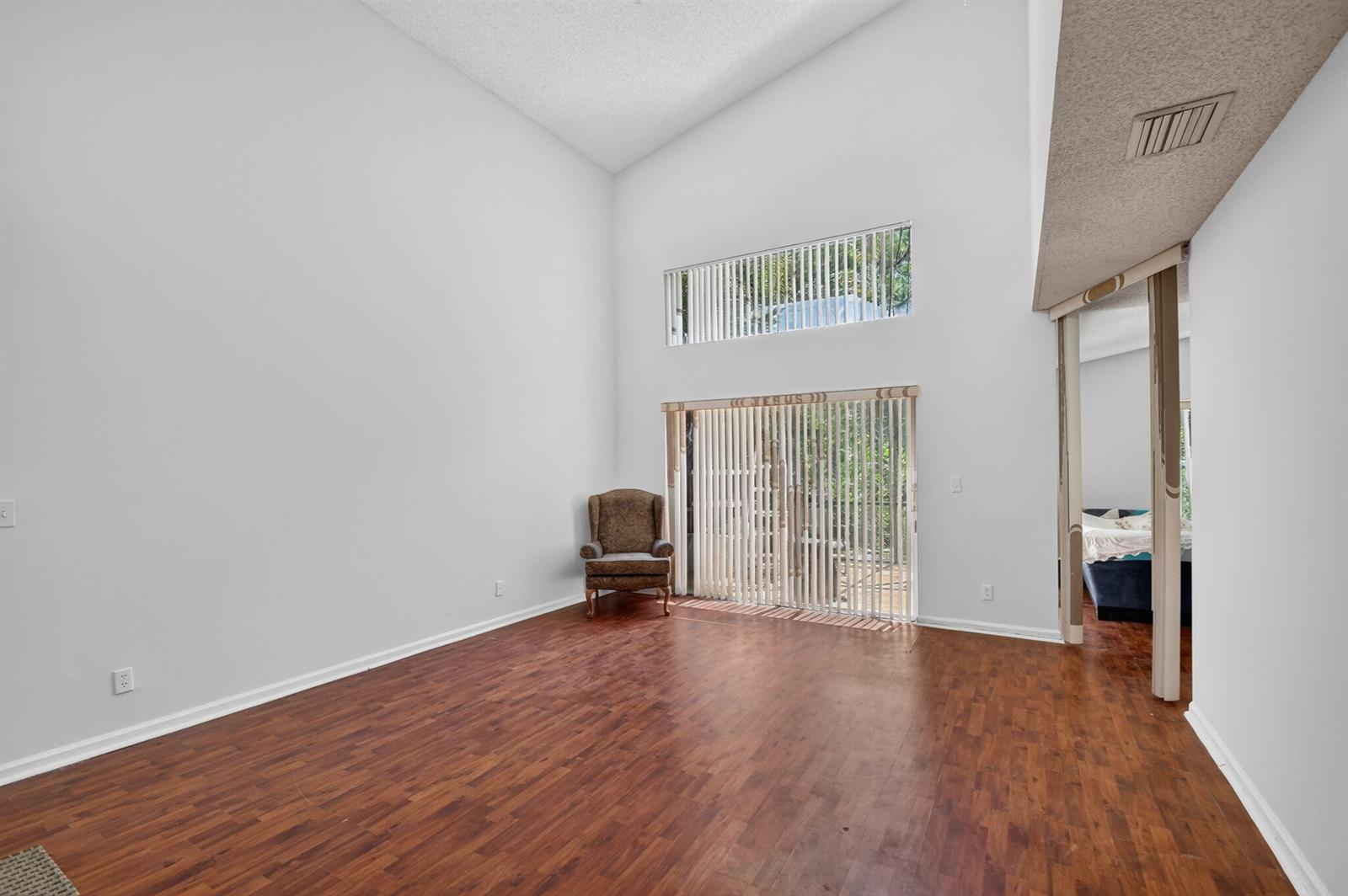 A living room with high ceilings, wood-look flooring, and a sliding glass door with blinds — 8332 Bermuda Sound Way, Boynton Beach FL 33436, BOYNTON BEACH, FL