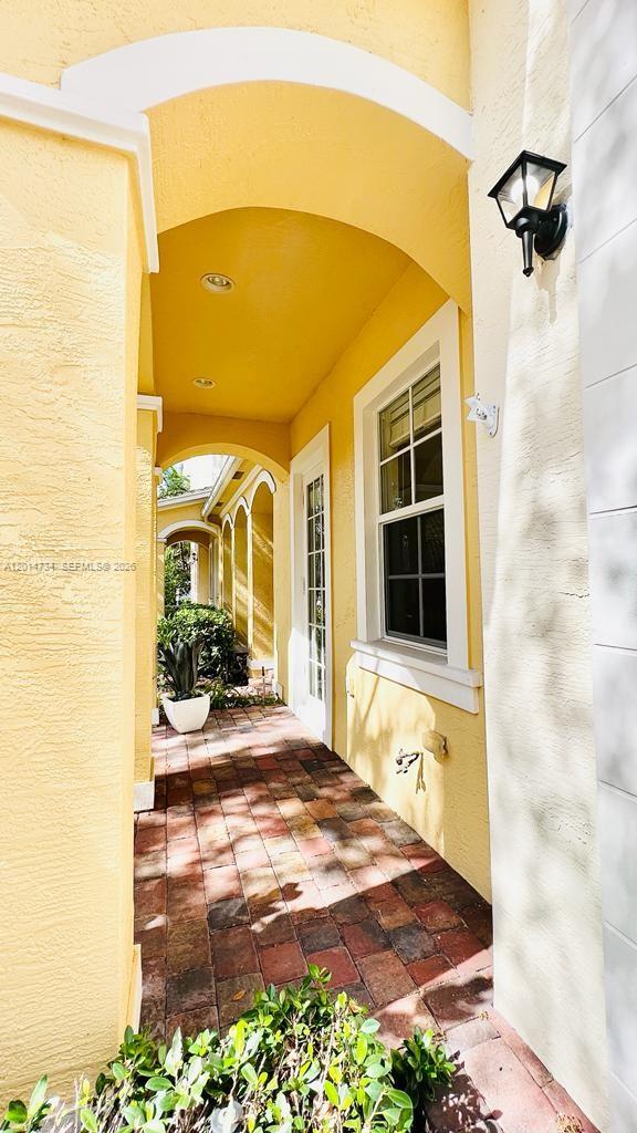 A covered walkway with yellow walls and a brick floor leads to a glass door — 753 DAKOTA DR # 753, Jupiter FL 33458, JUPITER, FL