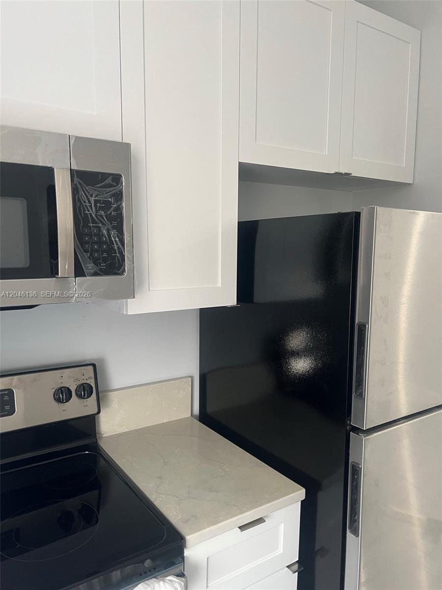 A kitchen features white cabinets, stainless steel appliances, a black refrigerator, and light countertops — 1450 SW 4th St # 3, Miami FL 33135, MIAMI, FL