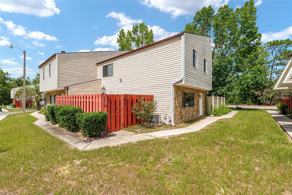 A two-story townhouse with beige siding, a stone facade, and a red wooden privacy fence — 2213 NE 45TH AVENUE, OCALA, FL