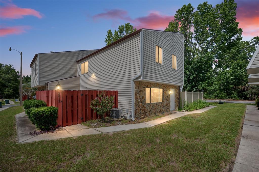 A two-story townhouse with beige siding, a stone facade, and a red wooden privacy fence — 2213 NE 45TH AVENUE, OCALA, FL