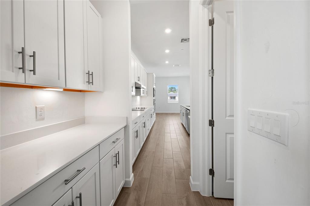 A white kitchen features light wood-look tile flooring and a long hallway leading to a window — 6020 MOUND KEY RUN, LAKEWOOD RANCH, FL
