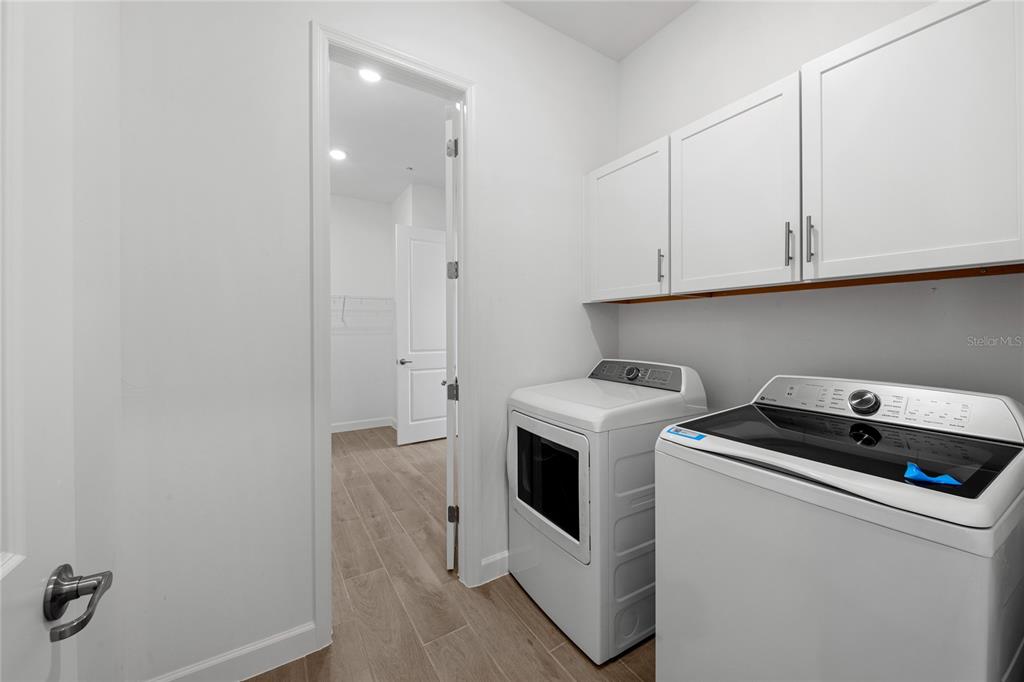 A laundry room features white cabinets, a washer and dryer, and a doorway to a closet — 6020 MOUND KEY RUN, LAKEWOOD RANCH, FL