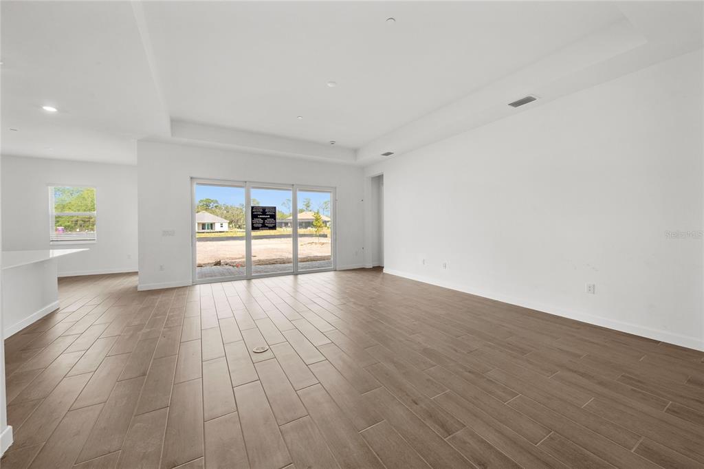 An empty living room features white walls, wood-look tile flooring, and sliding glass patio doors — 6020 MOUND KEY RUN, LAKEWOOD RANCH, FL