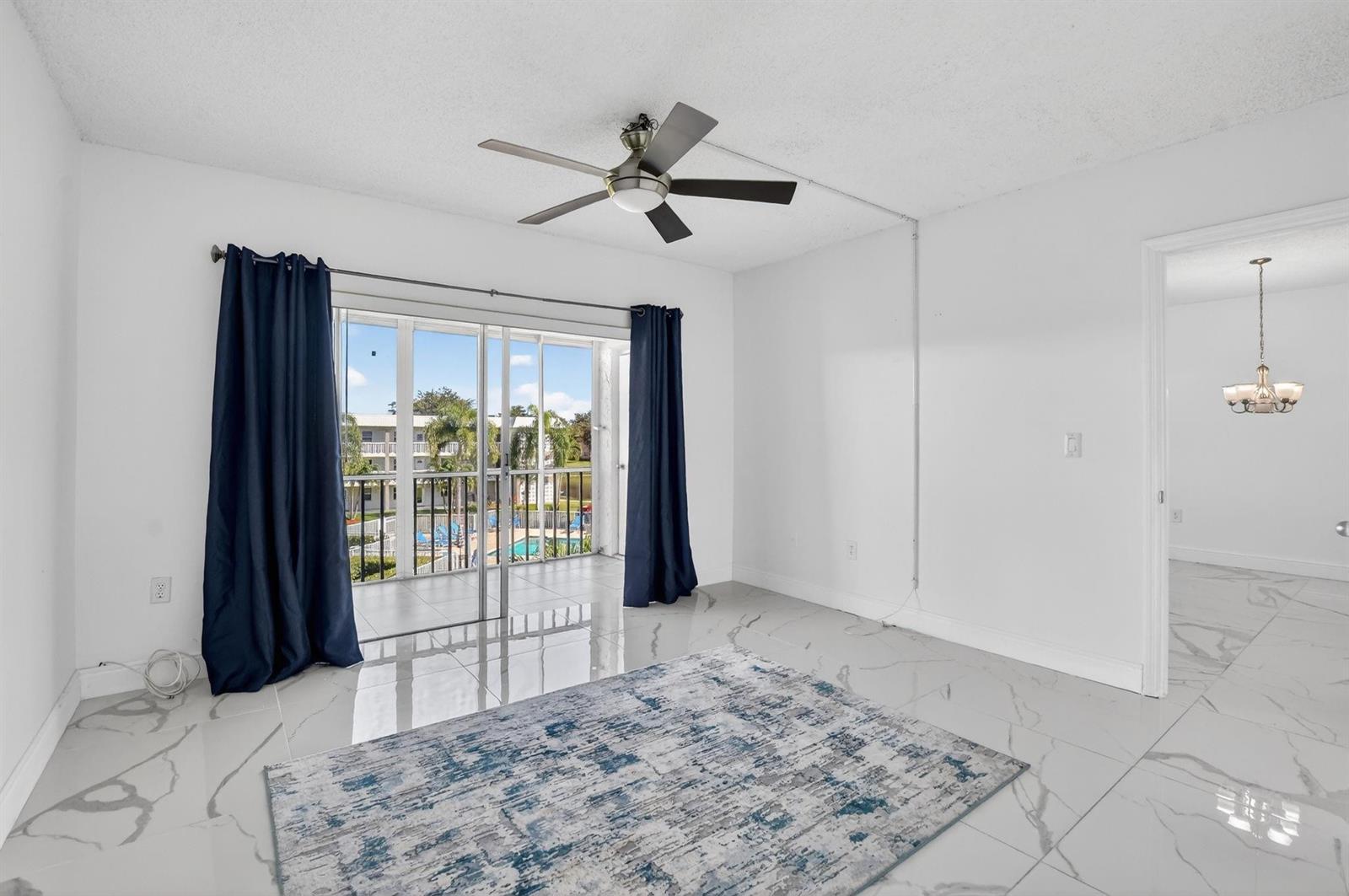A bright room features white marble-look tile floors, a ceiling fan, and sliding glass doors — 9872 Marina Boulevard # 1433, Boca Raton FL 33428, BOCA RATON, FL