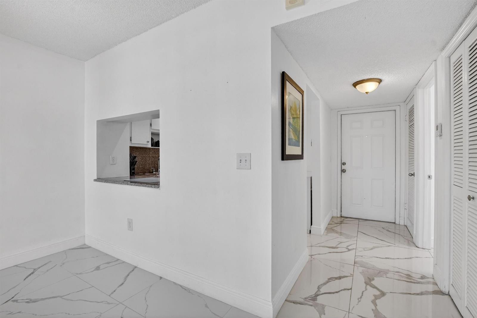 A hallway with white marble-look tile flooring leads to a white front door — 9872 Marina Boulevard # 1433, Boca Raton FL 33428, BOCA RATON, FL