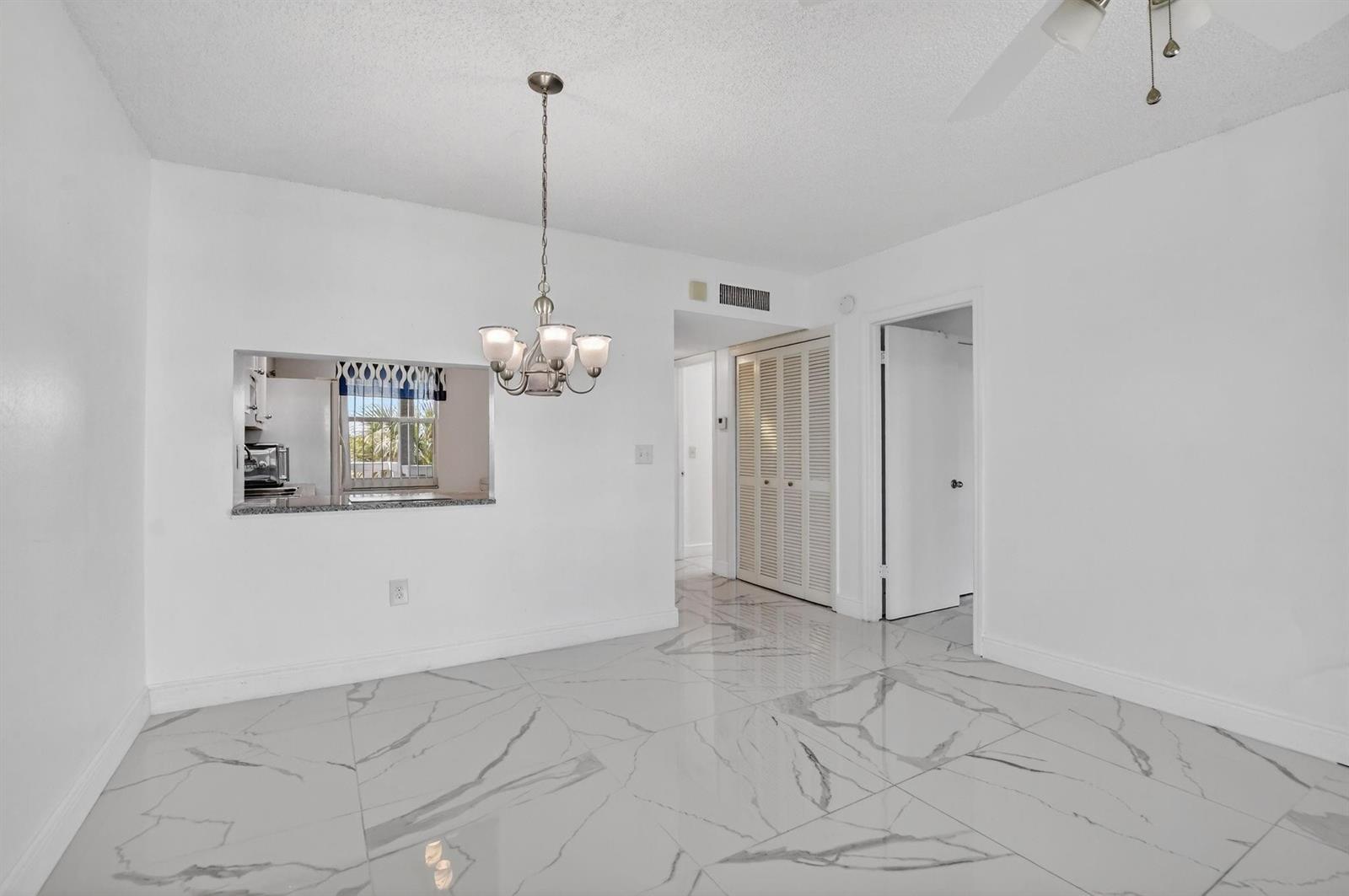 A dining area features white marble-look tile floors, a chandelier, and a kitchen pass-through window — 9872 Marina Boulevard # 1433, Boca Raton FL 33428, BOCA RATON, FL