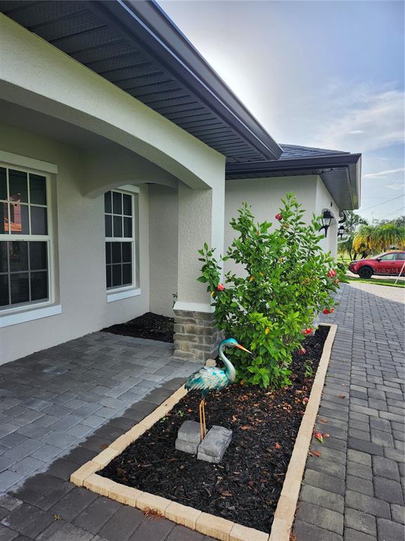 A paved walkway leads to a covered entryway with a landscaped bed and metal heron statue — 27270 PUNO DRIVE, PUNTA GORDA, FL