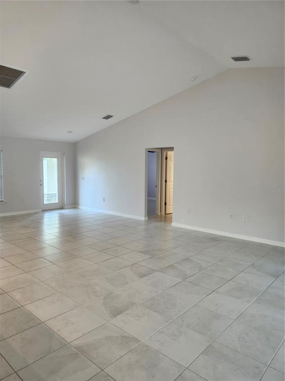 A spacious room features light gray tile flooring, vaulted ceilings, and a doorway leading inside — 27270 PUNO DRIVE, PUNTA GORDA, FL