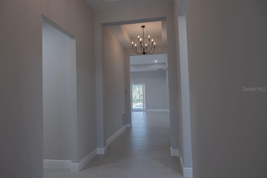 A hallway with light tile flooring leads to an open living area with a chandelier — 8100 SLIPWAY DRIVE, SARASOTA, FL