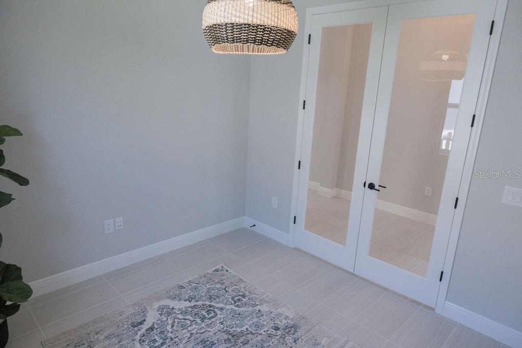 A room with light gray walls, tile flooring, a patterned rug, and white French doors — 8100 SLIPWAY DRIVE, SARASOTA, FL