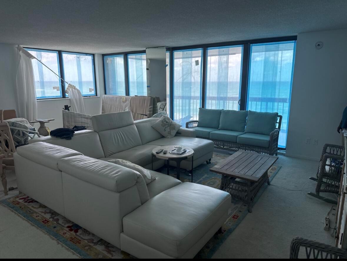 A living room with a large white sectional, wicker furniture, and floor-to-ceiling ocean view windows — 5380 N Ocean Drive # 4e, Singer Island FL 33404, SINGER ISLAND, FL