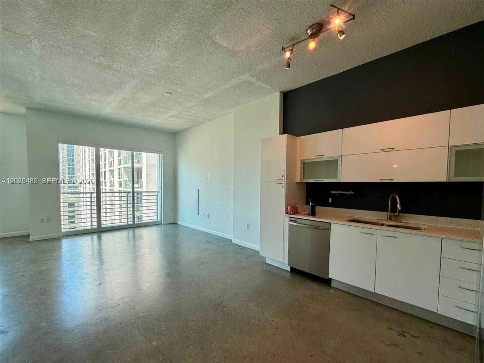 An open-concept kitchen with white cabinets and a stainless steel dishwasher overlooks a living area — 133 NE 2nd Ave # 1905, Miami FL 33132, MIAMI, FL