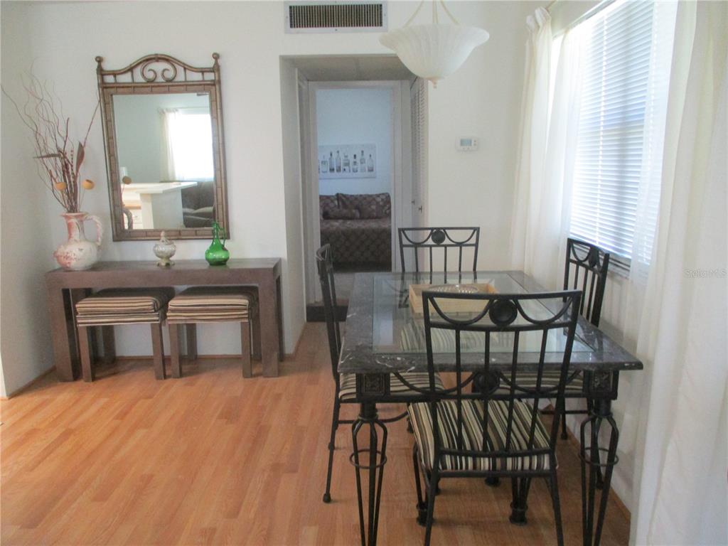 A dining area features a glass-topped table, metal chairs, a console table, and wood flooring — 101 CAMBRIDGE TRAIL UNIT 211, SUN CITY CENTER, FL