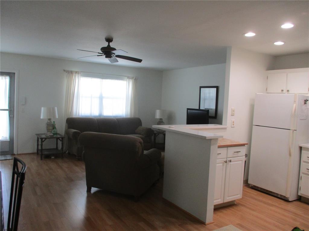 An open-concept living room and kitchen area featuring light wood flooring and white cabinetry — 101 CAMBRIDGE TRAIL UNIT 211, SUN CITY CENTER, FL