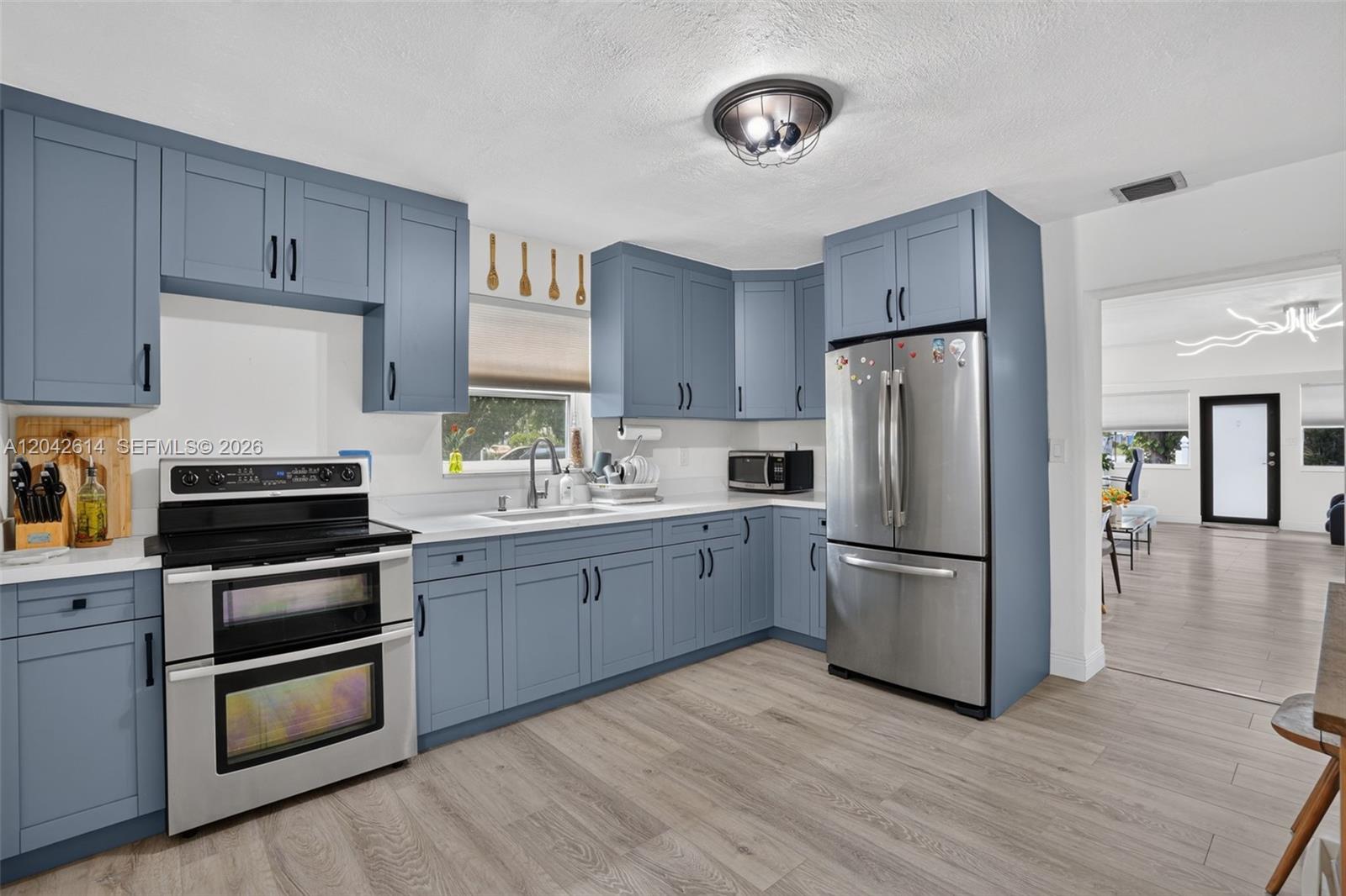 A kitchen features blue cabinets, stainless steel appliances, white countertops, and light wood-look flooring — 2446 Mckinley St, Hollywood FL 33020, HOLLYWOOD, FL