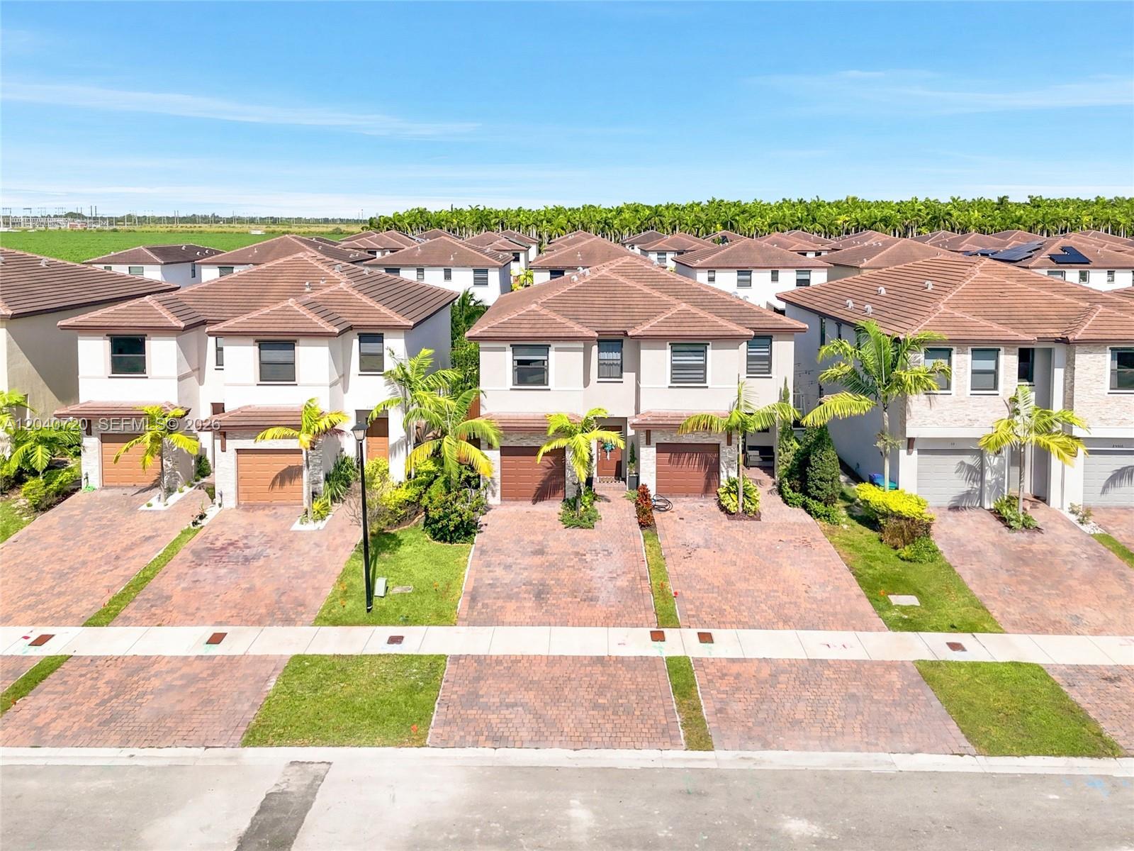 An aerial view shows a row of two-story suburban townhouses with brick driveways and palm trees — HOMESTEAD, FL